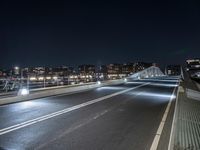 there is a street going over the bridge at night time with cars driving along it