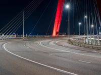 a red colored light in the night near a bridge at night, with a road on which is white lines