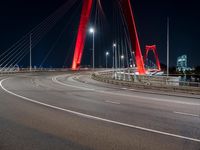 a red colored light in the night near a bridge at night, with a road on which is white lines