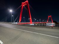 a red colored light in the night near a bridge at night, with a road on which is white lines