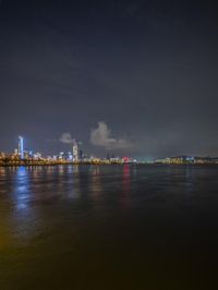 the skyline is lit up at night over a river or lake with the lights on