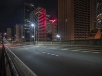 an empty roadway in a city at night in front of the skyscrapers or buildings