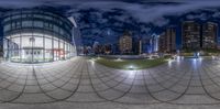 the 360 lens is reflecting city buildings at night time with traffic passing by at this street