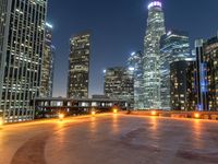 a very wide city at night and with tall buildings in the back ground, some empty benches, some benches and