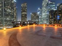 a very wide city at night and with tall buildings in the back ground, some empty benches, some benches and