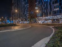 a paved street is shown at night near some very tall buildings on a street near trees