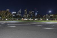 a empty street and some tall buildings and grass in the middle of a city at night