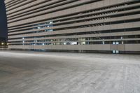 a concrete parking lot near several tall office buildings at night, some of which are empty