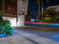 the building is surrounded by plants and plants, with light streaks on the road in the background