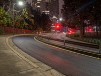 two streetlights that are on next to a curve road at night time with some buildings in the background