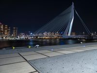 the bicycle rider is posing for a picture near the water at night, with a bridge in the background