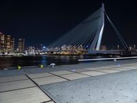 the bicycle rider is posing for a picture near the water at night, with a bridge in the background