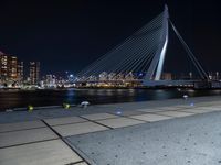 the bicycle rider is posing for a picture near the water at night, with a bridge in the background