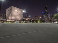 a nighttime view of a large city from the road area with empty parking lot and skyscrapers at the back