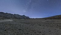 night sky over barren desert area under stars and clouds as seen from side of mountain