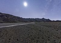 a moon shines brightly above a rocky landscape at night, a desert - like area full of dark gravel with rocks and sparse