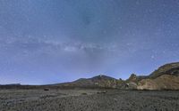 the stars above a mountainous desert plain under a clear night sky by the side of a hill