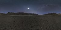 a view of the desert at night with the moon and stars in the sky and behind it there are mountains