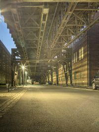 a car drives through an empty and deserted street at night, underneath an elevated overpass