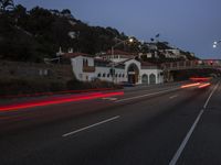 a car drives by a large white building and hill with many houses on it at night