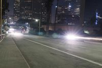 car driving down street with city buildings in the background at night time with light trails on side of roadway