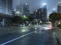 a street at night with fog covered city buildings in the background and car lights on