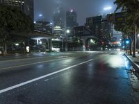 a street at night with fog covered city buildings in the background and car lights on