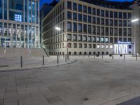 large circular stone parking area with stairs in front of buildings and street lights in the evening