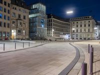 a night scene in a city with people walking around the plaza and sitting on benches