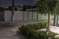 some bushes and a fence near a parking lot at night, with a stop sign next to it