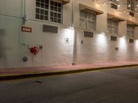 an empty city street at night with lights on the buildings behind it and two fire hydrants along the curb