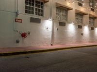 an empty city street at night with lights on the buildings behind it and two fire hydrants along the curb