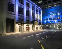 the empty street is lit up at night in front of a building with windows and doors