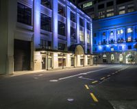 the empty street is lit up at night in front of a building with windows and doors