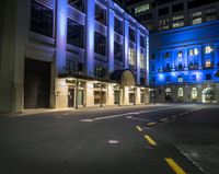 the empty street is lit up at night in front of a building with windows and doors