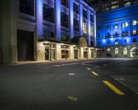 the empty street is lit up at night in front of a building with windows and doors