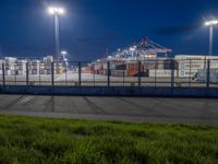 an empty parking lot with containers in the background at night time while a truck is on its way to dock