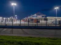 an empty parking lot with containers in the background at night time while a truck is on its way to dock