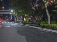 a street intersection at night with trees and lights on the side walk and some cars in the other road