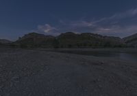 a full moon shines in the sky above a river and rocky shoreline at night