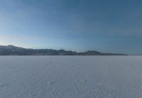 a lone skier is skiing across the open field of snow in the distance, with mountains and snow capped