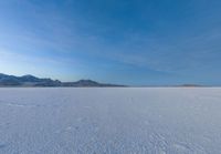 a lone skier is skiing across the open field of snow in the distance, with mountains and snow capped