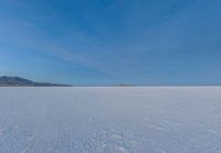 a lone skier is skiing across the open field of snow in the distance, with mountains and snow capped