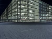 an empty road in front of a glass building at night with lights on it's windows