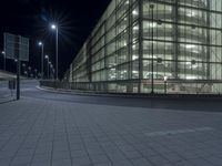 an empty road in front of a glass building at night with lights on it's windows