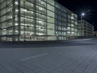 an empty road in front of a glass building at night with lights on it's windows