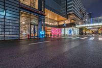 a city street with a storefront near by and buildings at night lights from windows