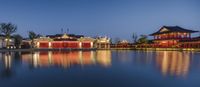 a pond that has red lights and some buildings in the background at night time with its reflection