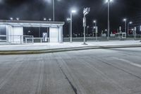 an empty parking lot at night time with stop lights on the side and lights on the other side of the street