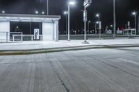 an empty parking lot at night time with stop lights on the side and lights on the other side of the street